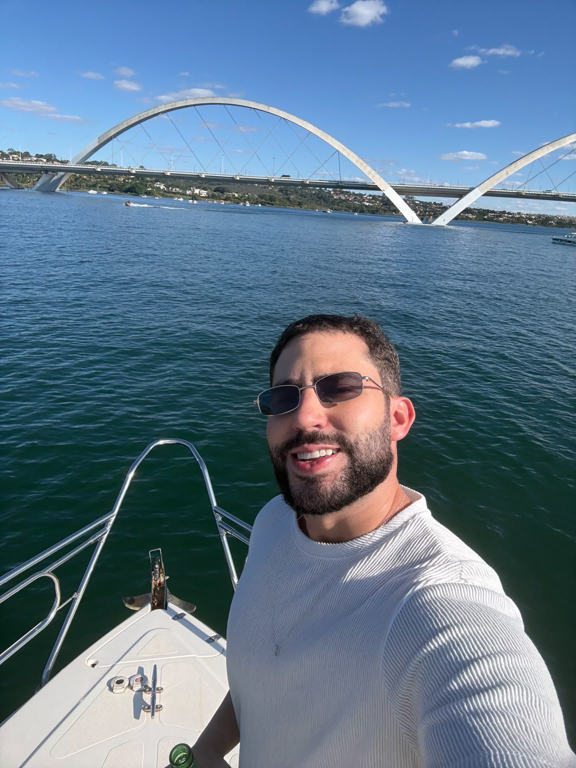 MAUG sorrindo em um barco no lago, com uma ponte em arcos ao fundo