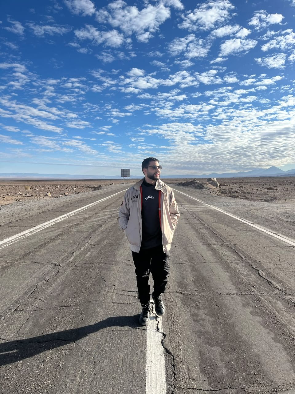MAUG caminhando no meio de uma estrada no deserto, sob um céu azul com nuvens