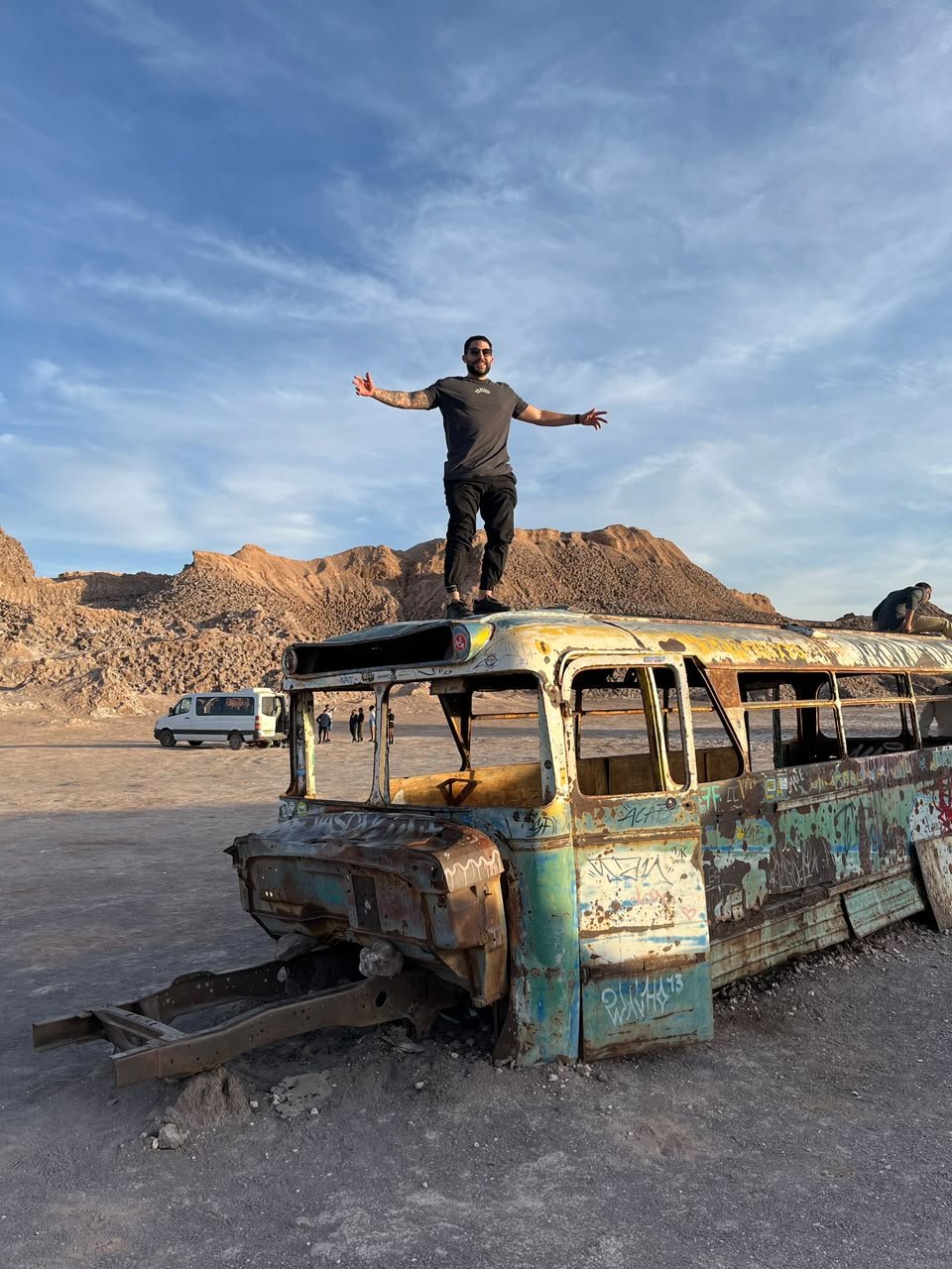 MAUG de braços abertos em cima de um ônibus antigo no deserto