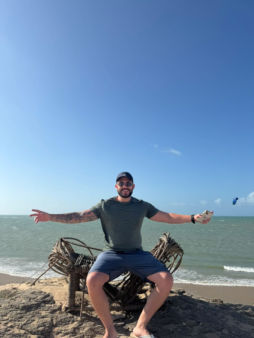 MAUG sentado em uma pedra na praia, de braços abertos